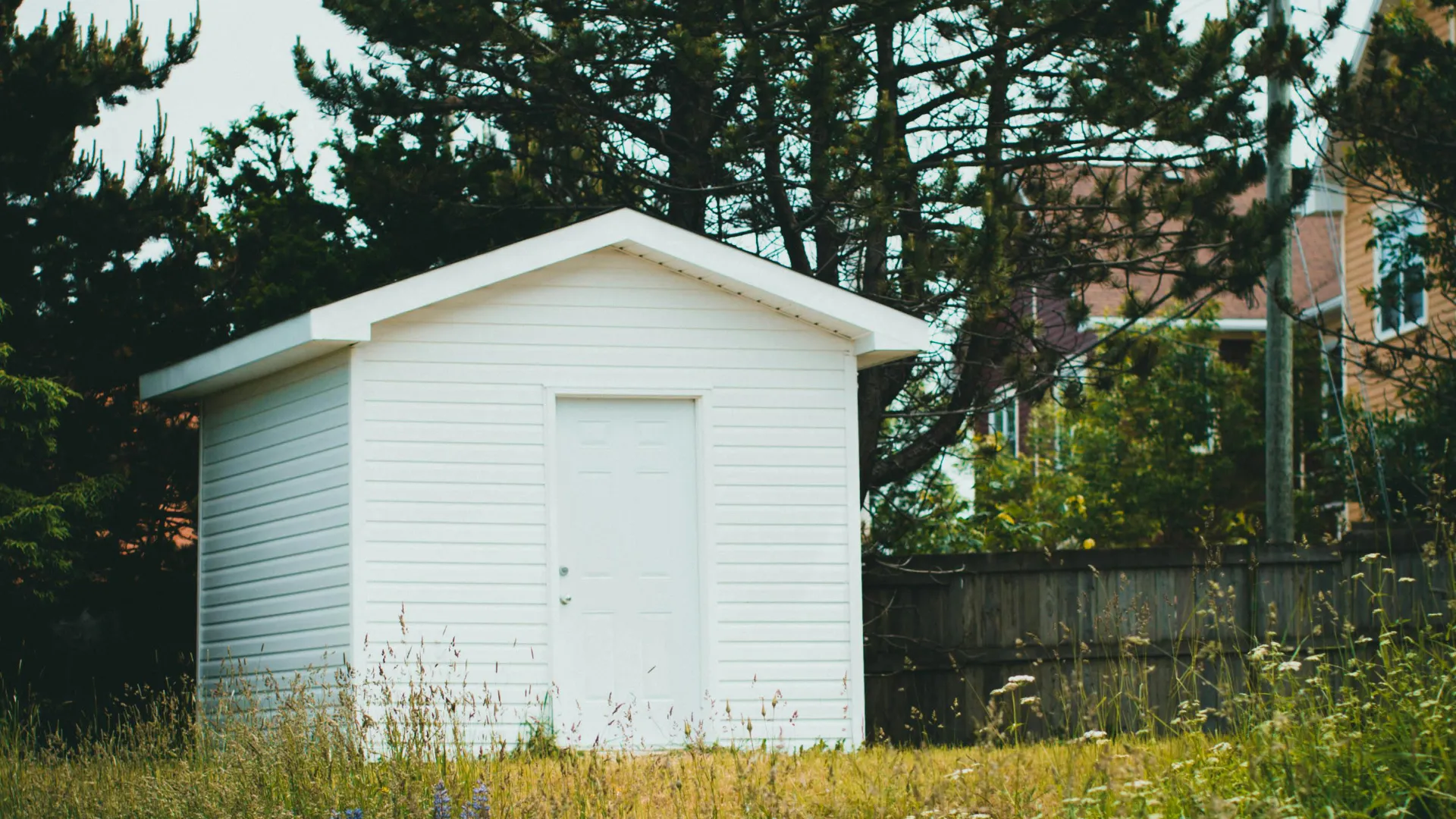 Biała drewniana szopa na działce przy domu jednorodzinnym w Szczecinie