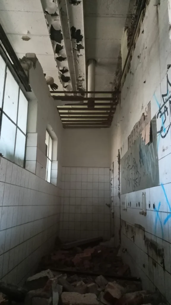 Wąskie i ciasne pomieszczenie – widać pierwsze zburzone cegły, rozbiórka budynku magazynowego w Szczecinie w trakcie prac.