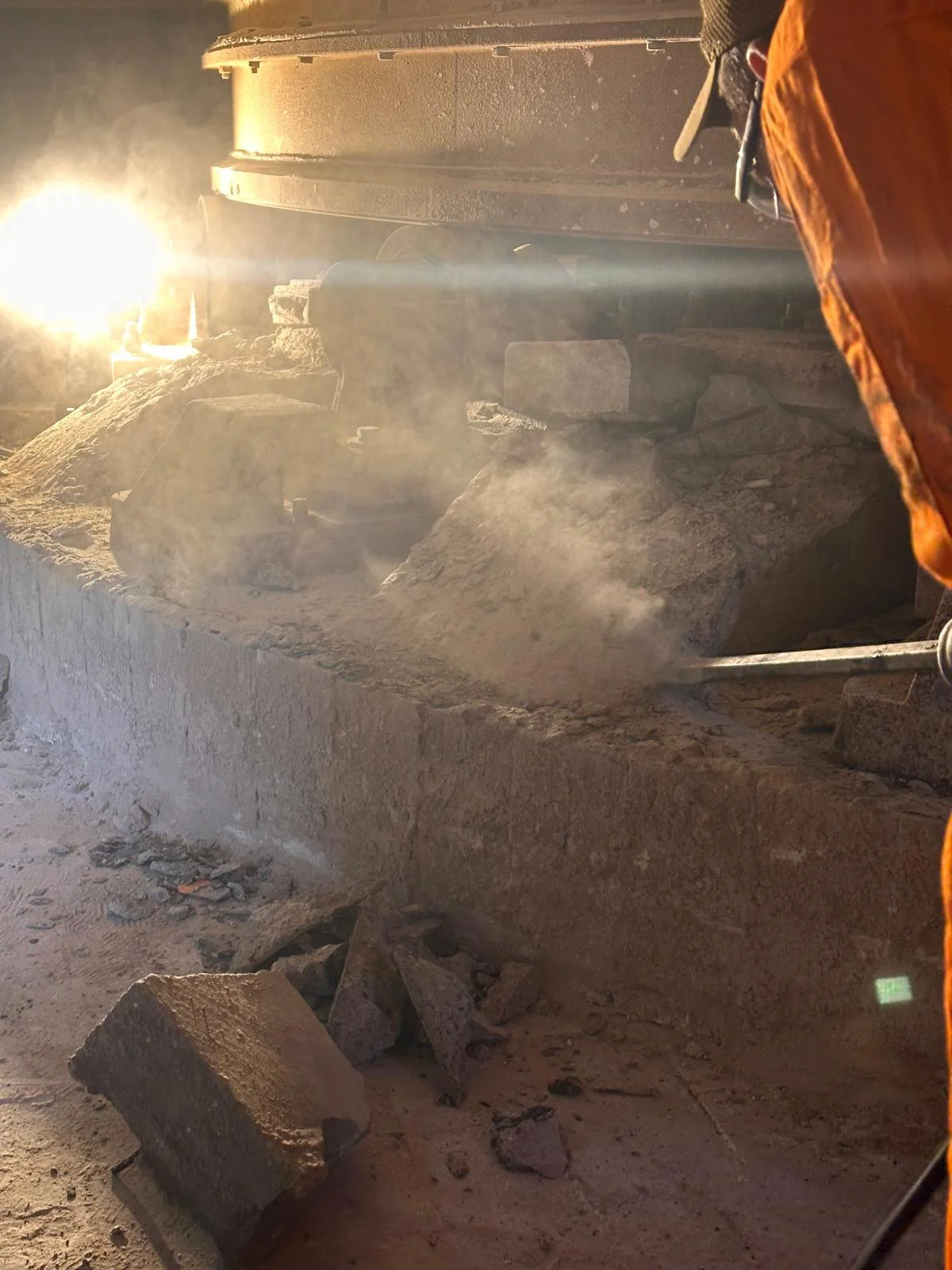 Zbliżenie na dłuto młota pneumatycznego skuwające fragmenty zdegradowanego betonu konstrukcyjnego, wokół którego unosi się gęsty pył.