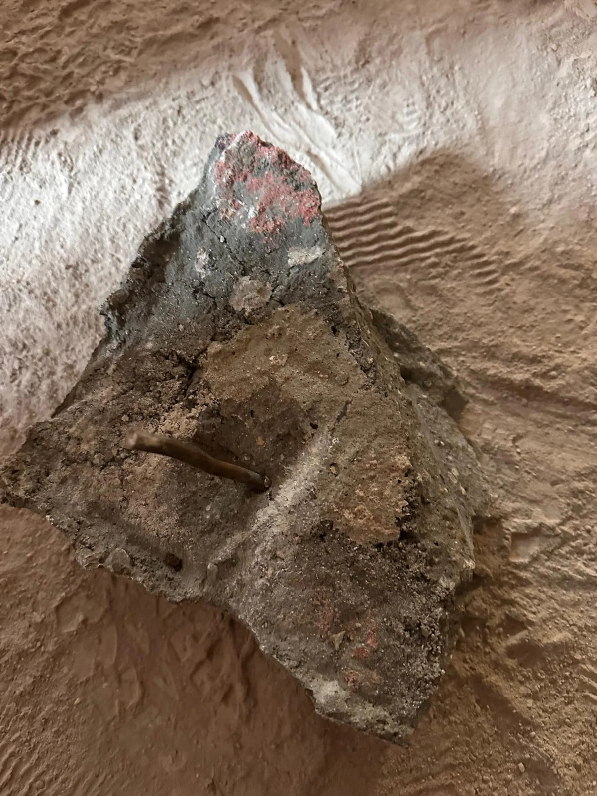 Odłupany, duży fragment zdegradowanego betonu z widoczną metalową kotwą montażową.