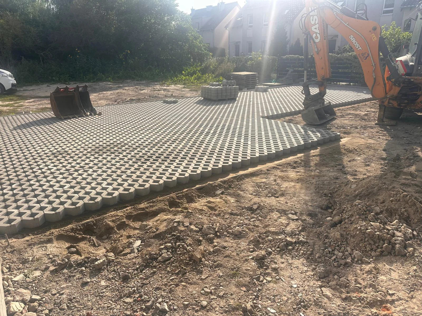 Widok na ułożoną nawierzchnię z betonowych płyt ażurowych na placu budowy w Szczecinie, z widoczną koparkoładowarką CASE i przygotowanym podłożem.